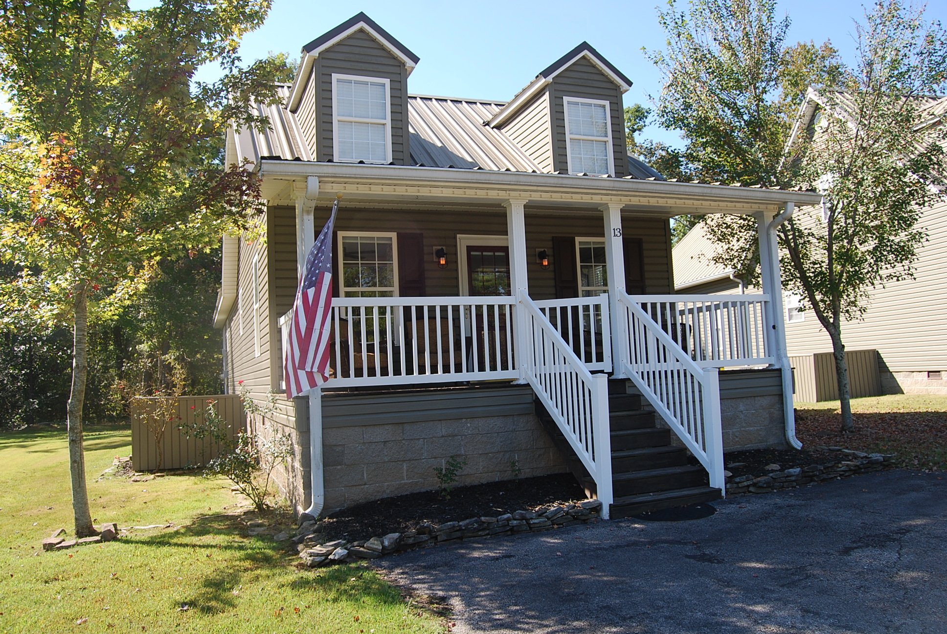 Front exterior of the home with its covered porch, white railing, steps, and lawn.